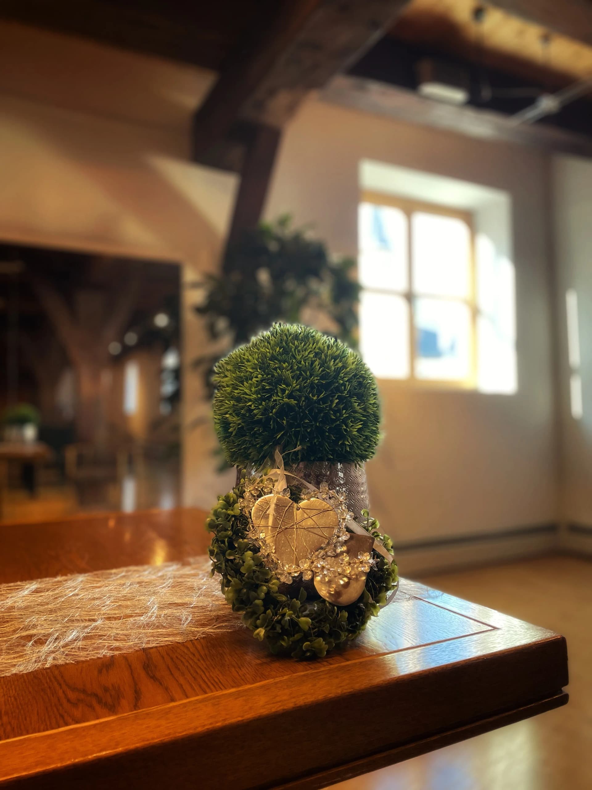 Grüne Tischdekoration mit Kunstbuchsbaumkugel auf einem Holztisch in der Kellereischeune