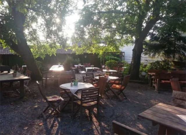 Biergarten mit Holztischen und Stühlen unter schattenspendenden Bäumen