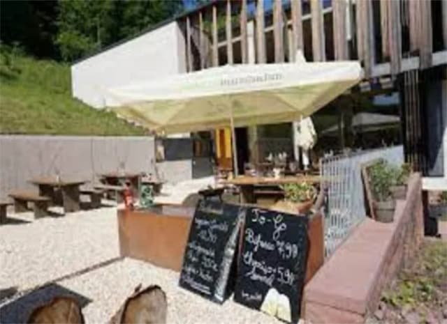 Terrasse eines Restaurants mit Sonnenschirm, Sitzbänken und Kreidetafeln mit Speiseangeboten