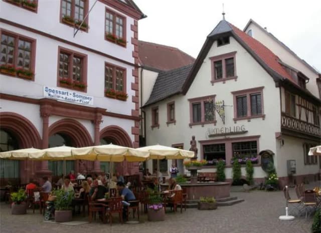 Marktplatz mit Fachwerkhäusern, Brunnen und Gästen unter Sonnenschirmen vor dem Gasthaus Mehling