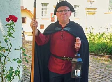 Mann in historischem Nachtwächter-Kostüm mit Hellebarde und Laterne vor einem Gebäude