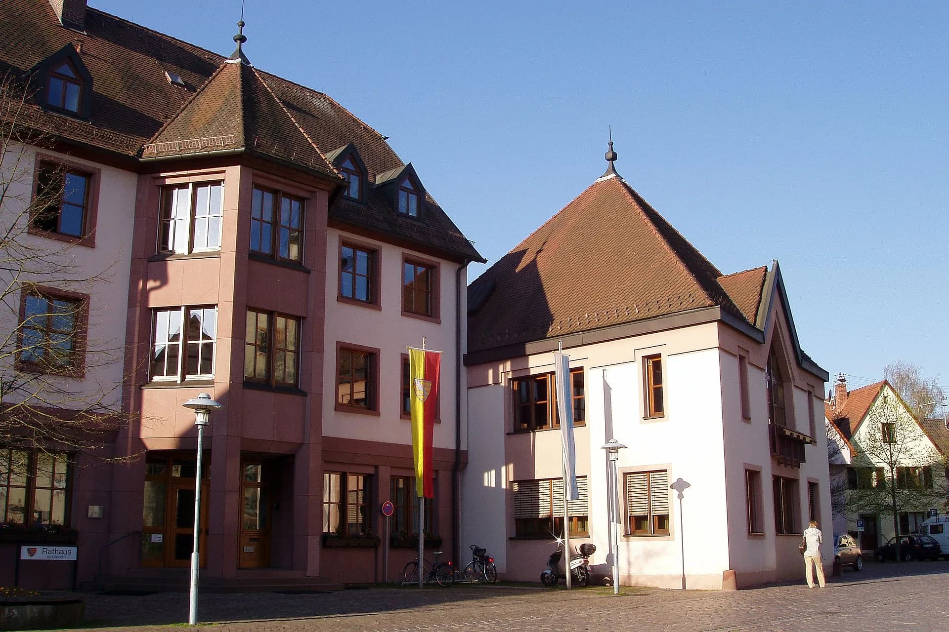 Rathausgebäude mit Walmdächern und Fahnenmasten an einem gepflasterten Platz