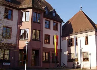Rathausgebäude mit rotem Fachwerk-Giebeldach, davor Fahnenmast mit Flagge und geparkte Fahrräder