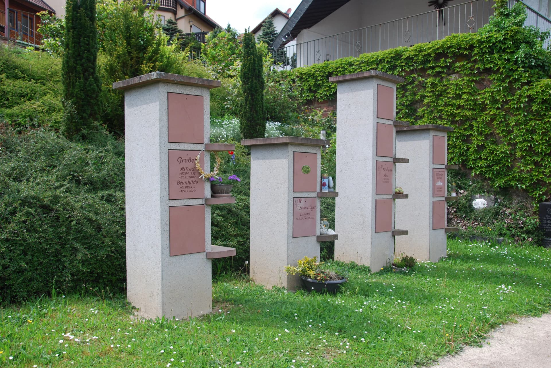 Steinstelen mit Namenstafeln auf einem Friedhof, umgeben von Rasen und Hecken