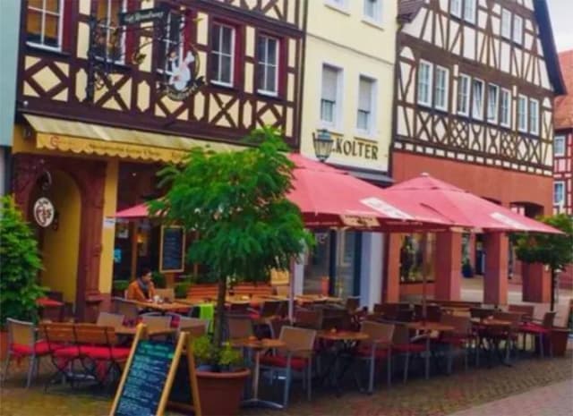 Straßencafé mit roten Sonnenschirmen vor Fachwerkhäusern, im Hintergrund ein Schild mit der Aufschrift Kolter