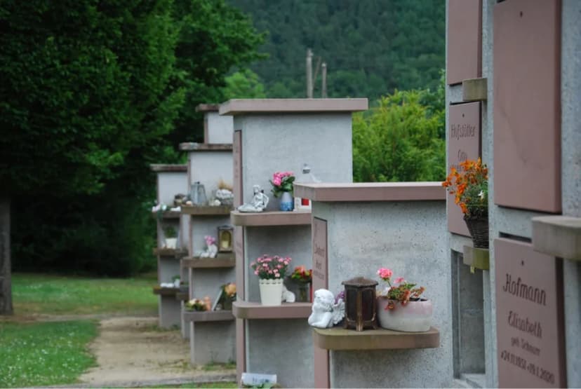 Reihe von Grabsteinstelen auf einem Friedhof mit Blumen, Grablichtern und Engelsfiguren