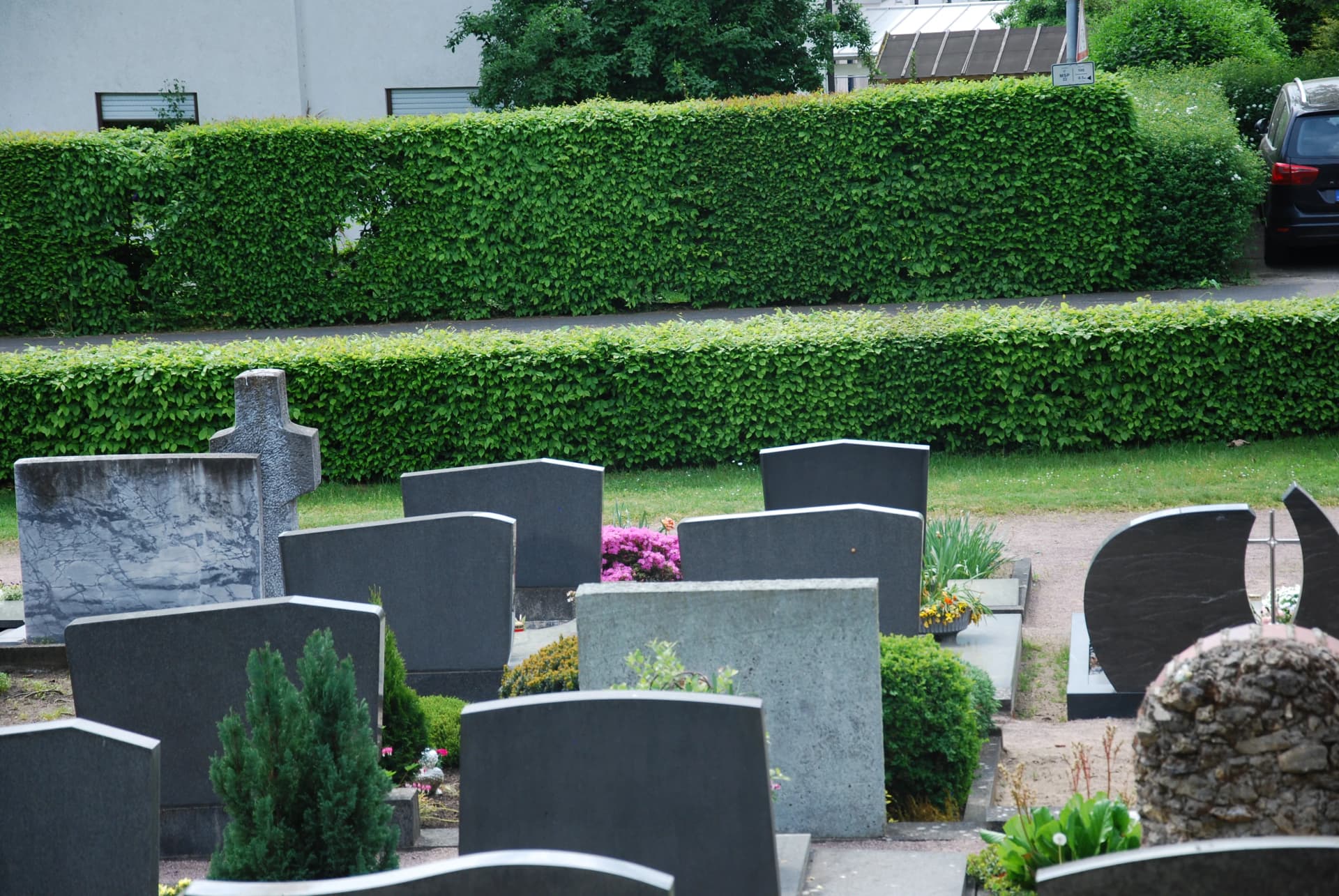 Grabsteine auf einem Friedhof mit bepflanzten Gräbern vor geschnittenen Hecken