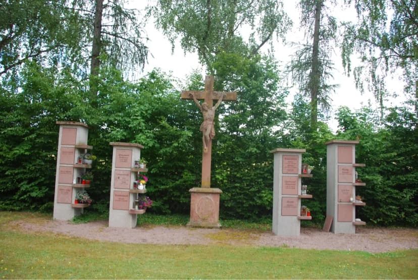 Steinernes Kruzifix zwischen Grabstelen mit Namenstafeln und Grablichtern auf einem Friedhof
