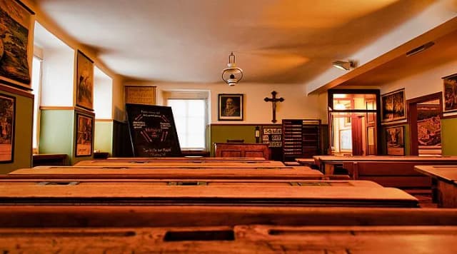 Historisches Klassenzimmer mit Holzbänken, Wandtafel, Kruzifix und alten Bildern an den Wänden
