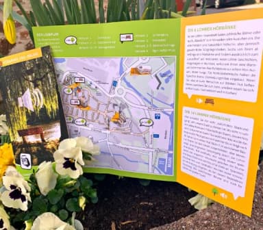 Der Flyer der Hörbänke und -bäume liegt dekorativ in einem Blumenbeet