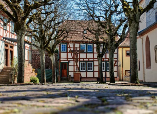 Kopfsteinpflasterplatz mit kahlen Bäumen vor einem Fachwerkhaus und einem Kruzifix davor