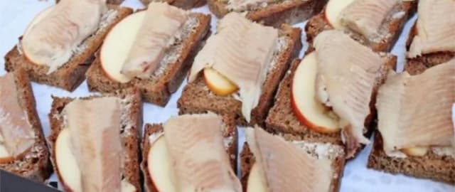 Häppchen aus Schwarzbrot mit Fischfilet und Apfelscheiben, reihenweise angerichtet