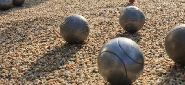Mehrere Metallkugeln für Pétanque liegen auf einem Kiesplatz.