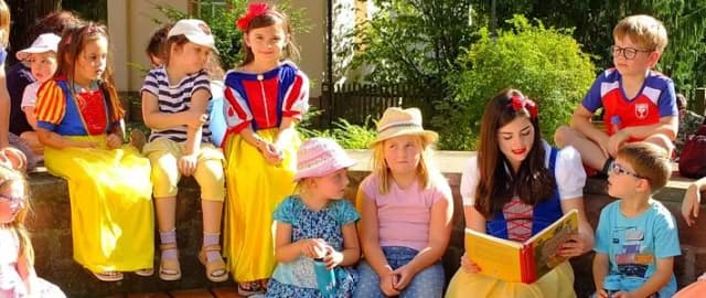 Das Lohrer Schneewittchen liest Kindern im Freien aus einem Märchenbuch mit Erzählungen der Brüder Grimm vor. Einige Kinder tragen ebenfalls Kostüme.