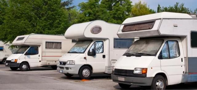 Mehrere Wohnmobile stehen nebeneinander auf einem Parkplatz.