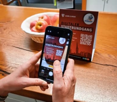 Jemand scaned mit dem SmartPhone den QR-Code auf dem Tischaufsteller für den Digitalen Stadtrundgang