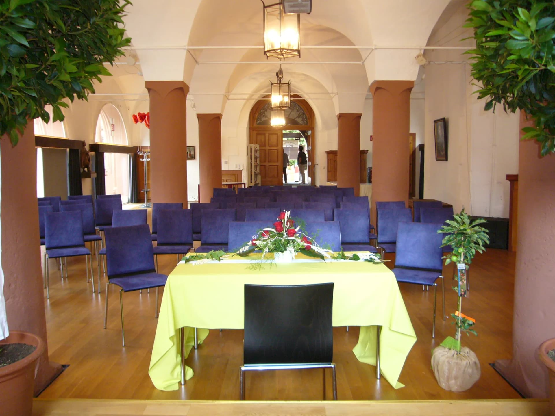 Trauraum im Alten Rathaus mit Gewölbedecke, blauen Stuhlreihen und einem gelb gedeckten Tisch mit Blumengesteck