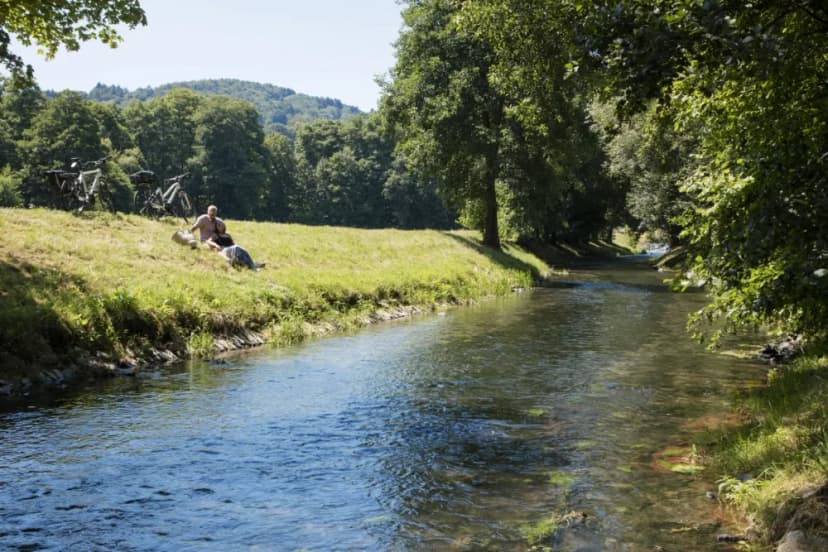 An der Ufer des Lohrer Naherholungsgebietes Wöhrde sitzen zwei Radfahrer, die eine Pause eingelegt haben. Ihr Blick geht auf den Fluss Lohr.