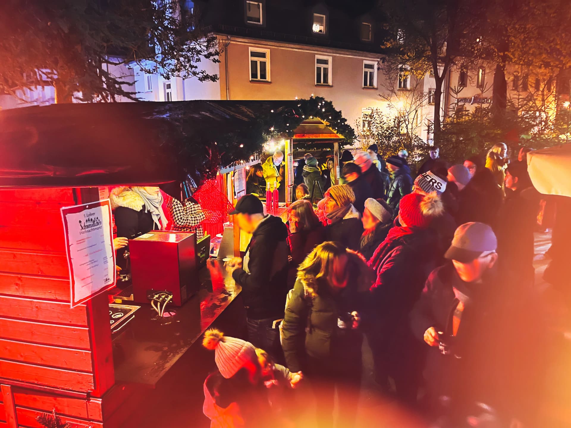 Menschen in Winterkleidung stehen abends an einem beleuchteten Verkaufsstand auf dem Weihnachtsmarkt in Lohr am Main.