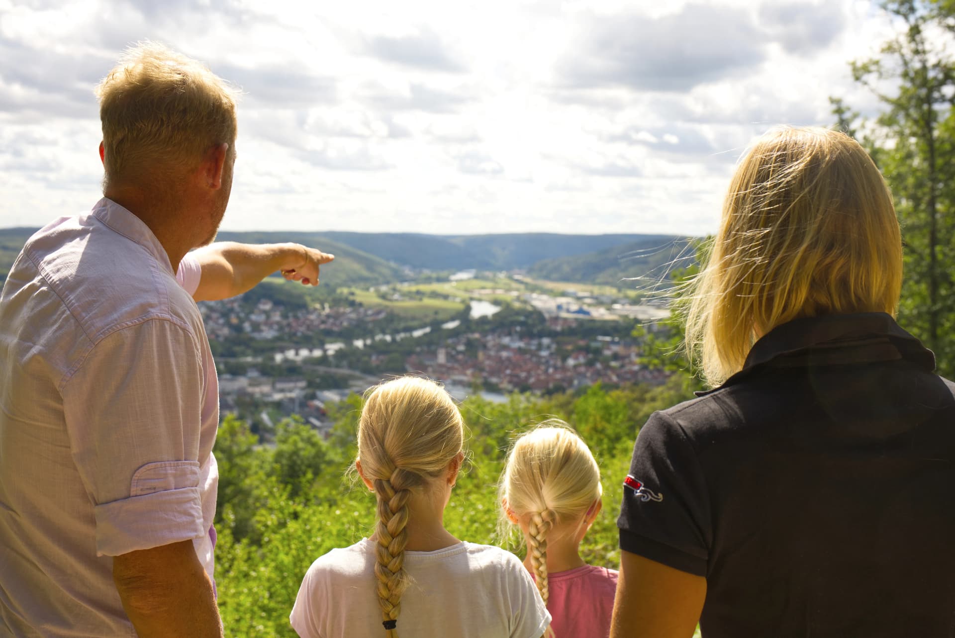 Eine vierköpfige Familie blickt vom Beilstein in Lohr auf die Stadt und genießt die Aussicht. Der Vater erklärt seinen zwei Töchtern etwas.