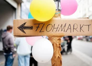 Pappschild mit Pfeil und Aufschrift Flohmarkt, umwickelt mit bunten Luftballons