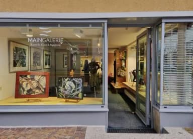 Schaufenster der Maingalerie mit ausgestellten Gemälden und geöffneter Eingangstür