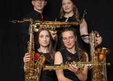 Vier Personen in schwarzer Kleidung posieren mit Saxophonen vor dunklem Hintergrund