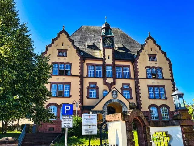 Historisches Schulgebäude mit Turmuhr und zwei Giebeln in Lohr am Main, davor befindet sich ein Parkplatzschild