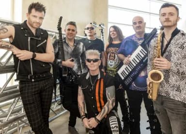 Gruppe von sieben Musikern einer Rockband mit Gitarre, Keyboard und Saxofon posiert für ein Bandfoto.