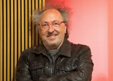 Mann mit Brille, grauen Haaren und Lederjacke lächelt mit verschränkten Armen in die Kamera