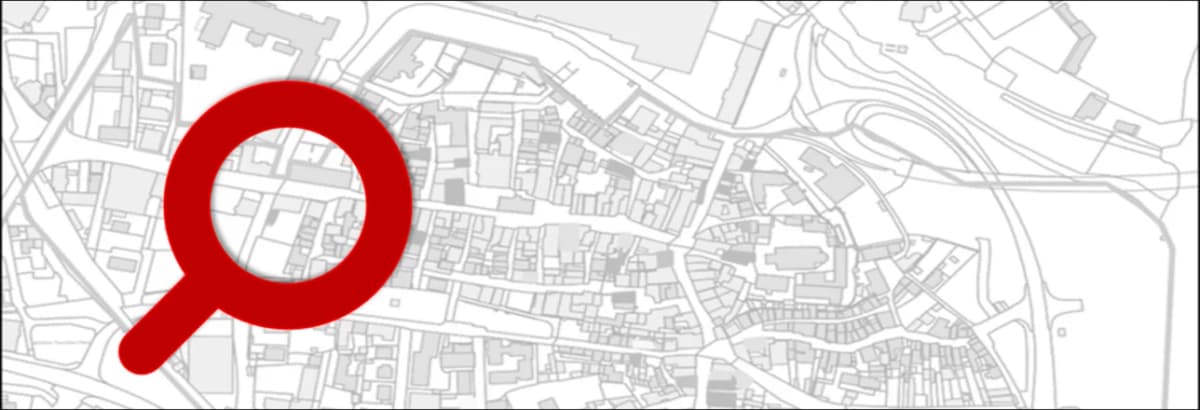Stadtplan-Ausschnitt mit Gebäudegrundrissen und einer großen roten Lupe als Symbol für Suche