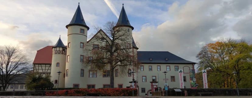 Schloss Lohr mit zwei runden Türmen und Fachwerkgiebel, davor herbstlich gefärbte Bäume