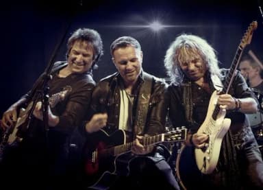 Bandmitglieder von Spirit of Smokie spielen mit Gitarren auf einer Bühne im Bühnenlicht