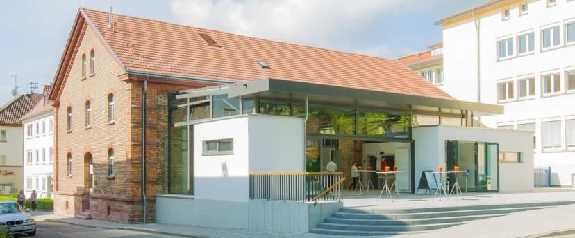 Sanierter Backsteinbau mit rotem Ziegeldach und moderner Glasanbau als Eingangsbereich, die Alte Turnhalle