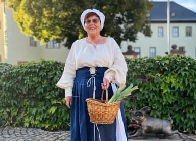 Frau in historischer Tracht mit Haube und Weidenkorb steht vor einem Schloss