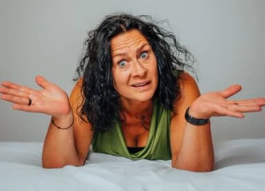 Frau liegt auf einem Bett und macht mit hochgezogenen Schultern eine ratlose Geste mit beiden Händen
