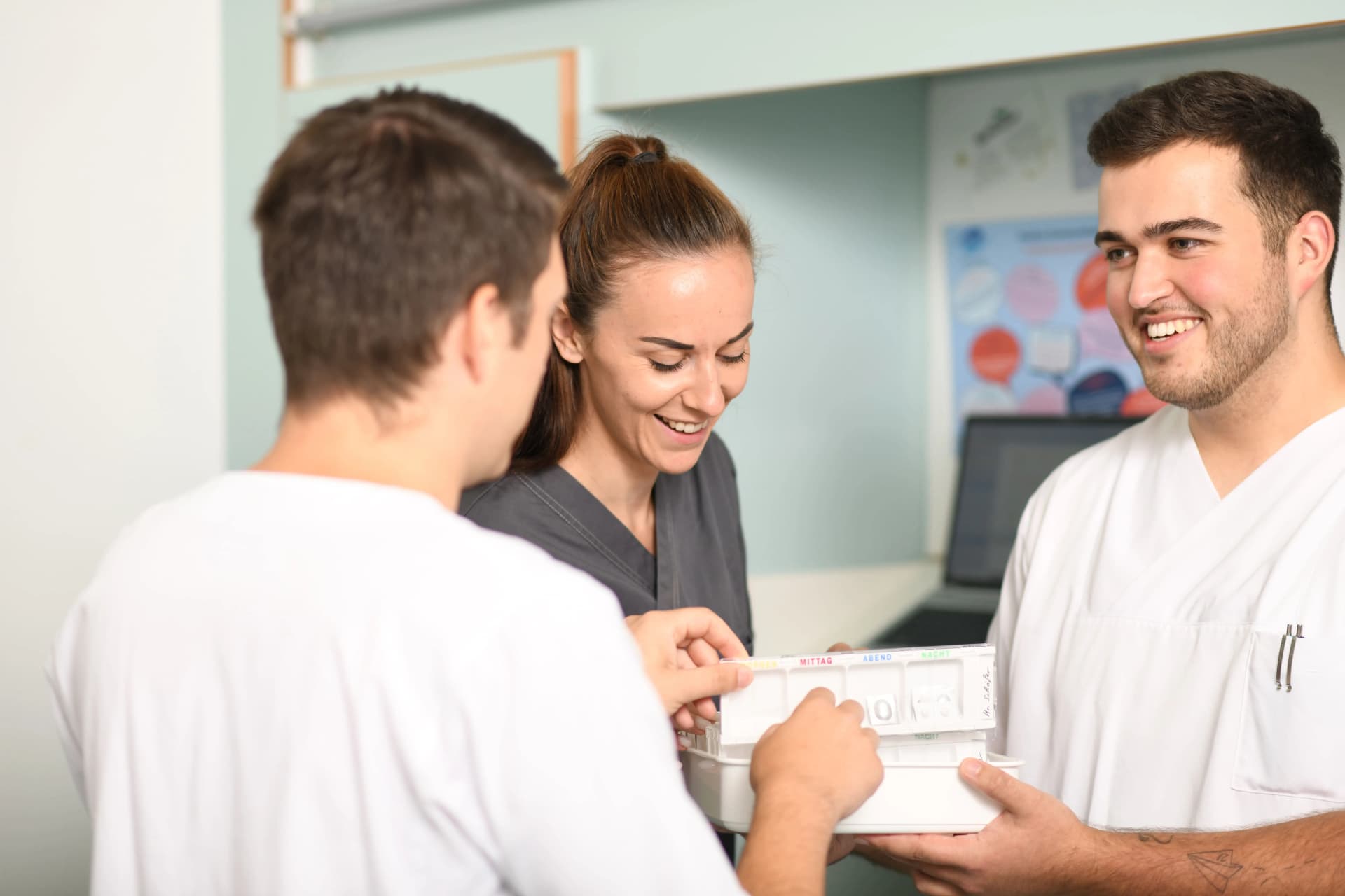 Auf dem Bild sind drei Pflegekräfte zu sehen, die Medikamente für einen Patienten richten.