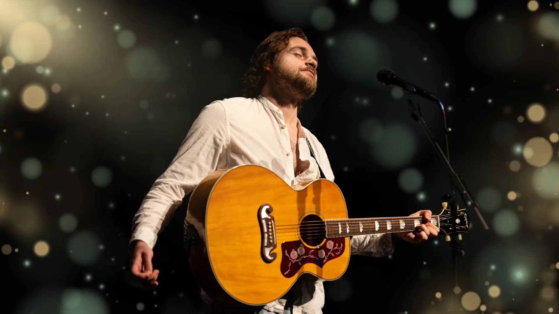 Der Sänger Patrick Snow steht mit geschlossenen Augen und Gitarre an einem Mikrophon