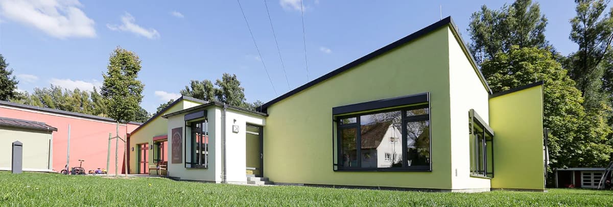 Eingeschossiges Kindergartengebäude mit grün-weißer Fassade und Rasenfläche davor