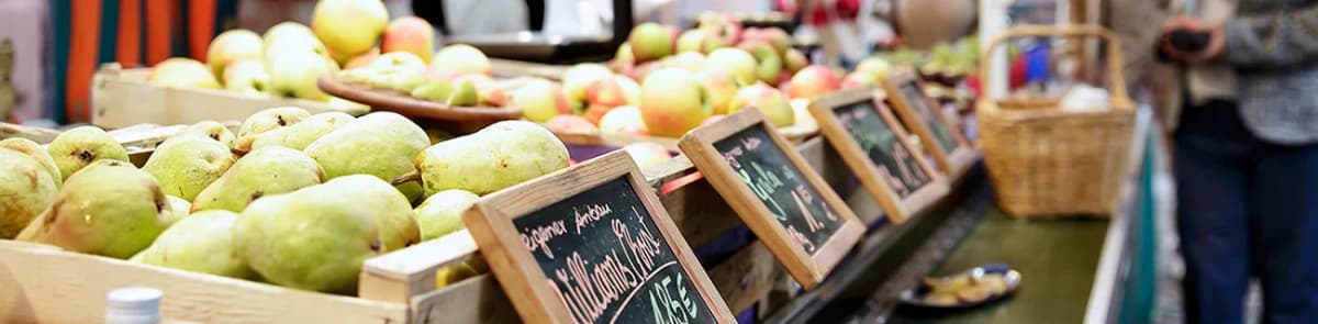 Marktstand mit Kisten voller Birnen und Äpfel, davor Preisschilder aus Tafeln