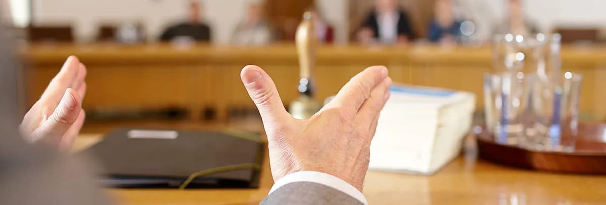 Gestikulierende Hände am Rednerpult im Sitzungssaal, im Hintergrund unscharf sitzende Personen