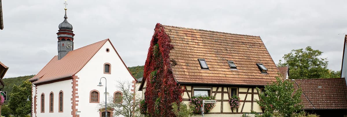 Kirche mit Zwiebelturm und Fachwerkhaus mit rot beranktem Giebel in Rodenbach