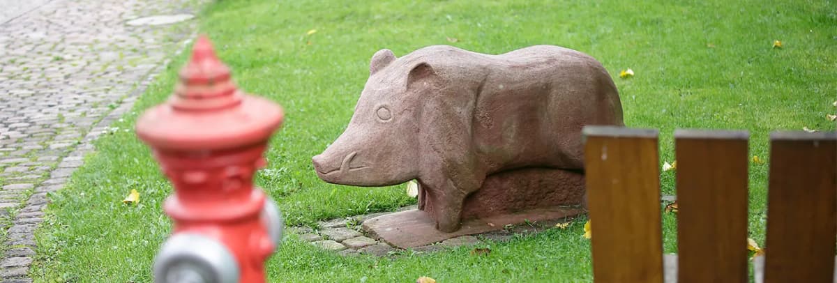 Steinskulptur eines Wildschweins auf einer Rasenfläche neben einem roten Hydranten