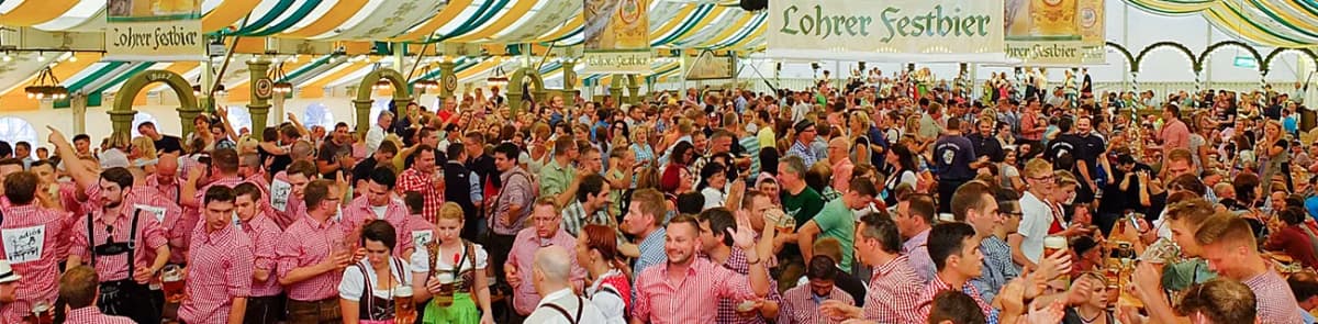 Volles Festzelt auf der Spessartfestwoche. Viele Feiernde sind in Tracht zu sehen, im Hintergrund befindet sich ein Banner mit der Aufschrift Lohrer Festbier.