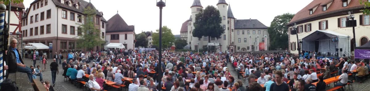 Menschenmenge auf dem Marktplatz mit Schloss im Hintergrund bei einer Veranstaltung mit Bühne und Bierbänken