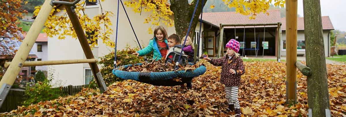 Kinder spielen im Herbstlaub auf einer Nestschaukel auf einem Spielplatz