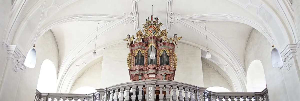 Barocke Orgel mit vergoldeten Verzierungen und Engelsfiguren auf der Empore einer Kirche mit Stuckdecke