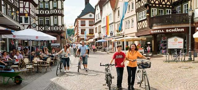 Fußgängerzone mit Fachwerkhäusern, Passanten mit Fahrrädern und Café-Tischen im Freien