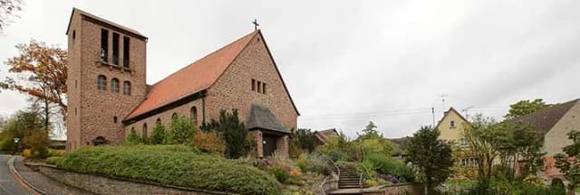Backsteinkirche mit Glockenturm und rotem Satteldach, umgeben von Gärten und Treppenaufgang