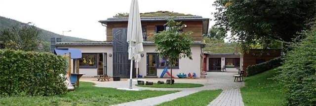 Kindergarten mit Gründach, Spielgeräten und Garten mit Sonnenschirm